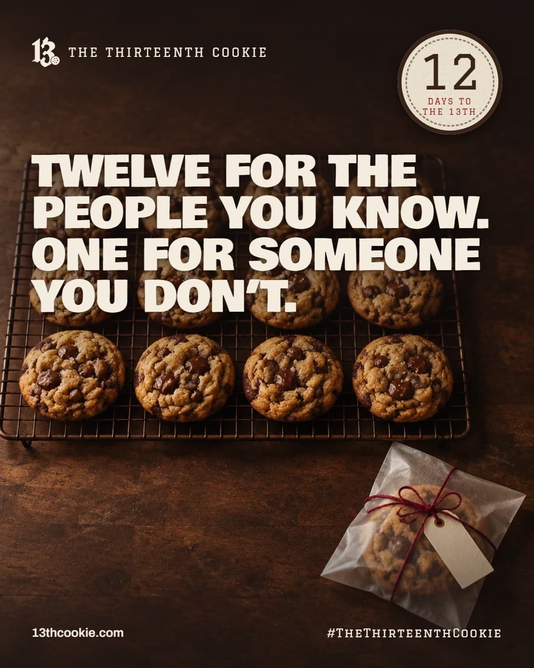 Twelve chocolate chip cookies cooling on a rack, and a thirteenth set apart in a paper sleeve with a tag.