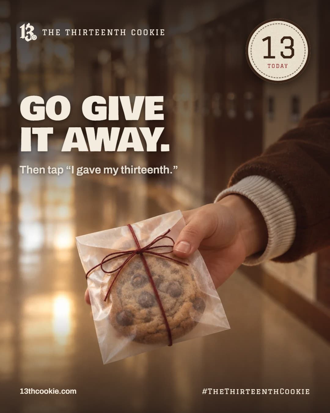 A hand in a cocoa varsity sleeve holding out a cookie in a paper sleeve, in a school hallway.